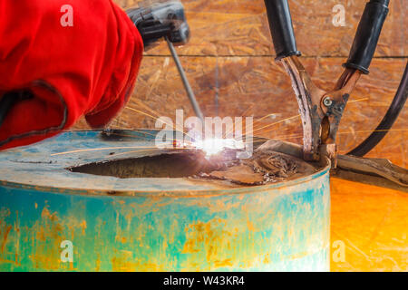 Lavoratore con Red Glove per proteggere la scintilla di luce con processo di saldatura con tubo blu metallico e luminose scintille in acciaio Foto Stock