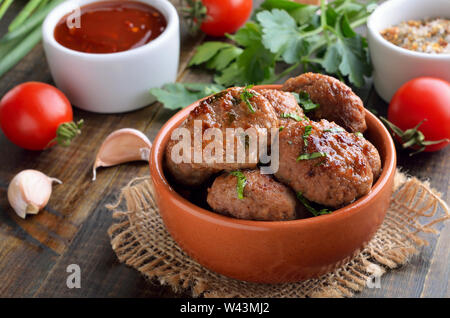 Polpette fritte in una terrina di prezzemolo fresco, pomodoro e salsa di pomodoro sulla tavola di legno, vista ravvicinata Foto Stock