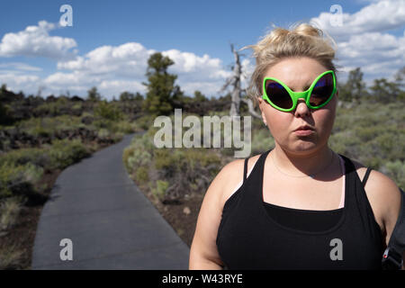Donna bionda indossando occhiali da sole alieno pone a crateri della luna Monumento Nazionale in Idaho. Concetto per extraterrestrial Foto Stock