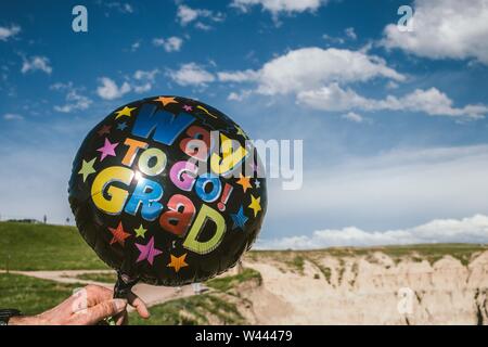 Primo piano di un palloncino nero con una scritta 'modo di Go Grad' tenuto da una persona nel deserto Foto Stock