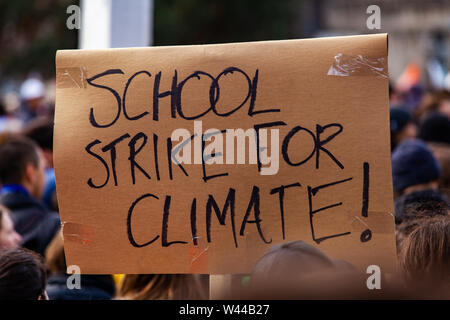 Un segno di cartone, lettura sciopero della scuola per il clima è visto closeup come attivisti ecologici unite contro il riscaldamento globale durante una pacifica manifestazione in strada Foto Stock