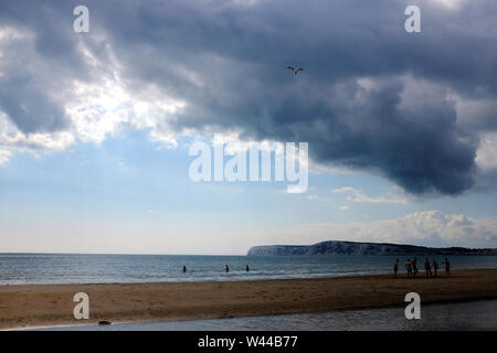 Un gruppo di persone che giocano a calcio sulla spiaggia di sabbia con la bassa marea e nuotando in lontananza sulla spiaggia di Compton, Compton, Isola di Wight Foto Stock