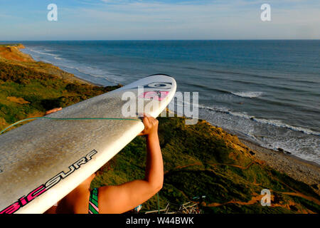 Una giovane donna porta la sua tavola da surf sulla sua testa come lei capi giù per le scale per andare in surf Compton Chine, Compton Bay, Isola di Wight Foto Stock