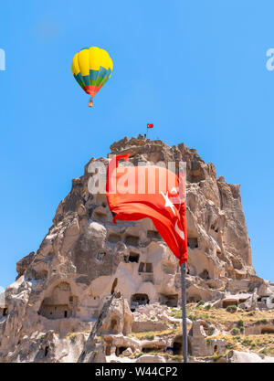 Messa a fuoco selettiva di Uchisar castello, uno dei più famoso punto di riferimento in Turchia con bandiera turca e una mongolfiera appena al di sopra del castello. Foto Stock