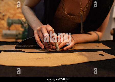 Sarta esperta è visto closeup, utilizzando strumenti per tagliare le forme dal tessuto. Modello di un nuovo abito steso sulla superficie di lavoro in atelier. Foto Stock