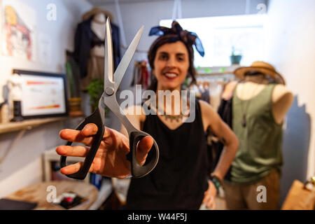 Un quartiere alla moda di sarta viene visto dalla parte anteriore tenendo un paio di forbici per la creazione all'interno di un atelier. Persona creativa che mostra gli strumenti di commercio. Foto Stock