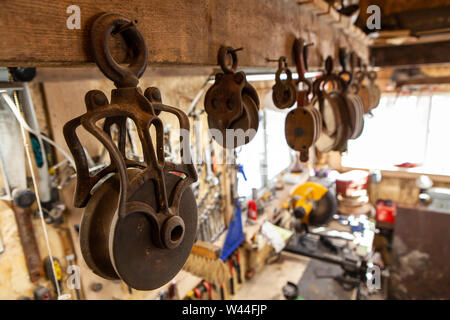 Un primo piano vista sul vecchio arrugginito pulegge appeso ad una trave di legno all'interno di una lamiera garage. Oggetti tradizionali utilizzati per il sollevamento di pesi pesanti. Foto Stock
