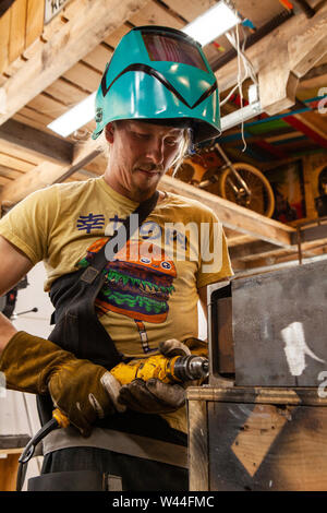 Un basso angolo di visione di un lavoratore metalmeccanico caucasica concentrando sulla perforazione di un foro con un trapano attraverso pesanti travi in acciaio. Operaio specializzato in opere Foto Stock