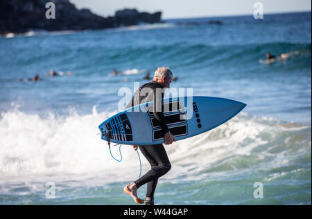 Il maschio australiano di mezza età in muta si dirige verso l'oceano per un surf, Sydney, Australia Foto Stock