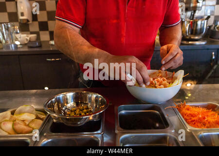 Un uomo è visto da vicino, preparare un insalata di gamberi da ingredienti freschi nella cucina di un moderno bistro, lo chef prepara antipasti per patroni Foto Stock