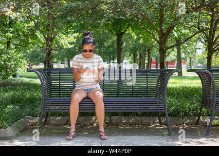 Una ragazza adolescente controlla il suo telefono cellulare mentre si è in attesa su una panchina nel parco a tre fiumi Festival in Fort Wayne, Indiana, Stati Uniti d'America. Foto Stock