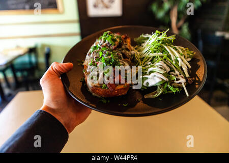 Un cameriere serve appena preparato la cena della bistecca di tonno e insalata all'interno di un moderno bistro, la prospettiva in prima persona come egli porta a una tabella. Foto Stock