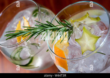 Angolo basso close up di ghiaccio freddo moderne imbarcazioni gourmet cocktail di gin tonic soda guarnita da fetta di limone e rosmarino rametto irrorato da Juniper essere Foto Stock
