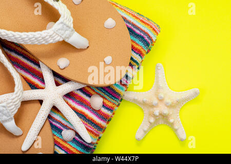 Donna causale colore naturale spiaggia Flip Flop e a strisce colorate telo da spiaggia decorato con dito bianco di stelle marine e conchiglie su sfondo giallo Foto Stock
