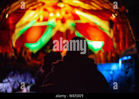 Una vista retroilluminato di persone a music festival che celebra la cultura dei nativi e moderni suoni, luci colorate sono sfocate in background di notte su un uomo di testa Foto Stock