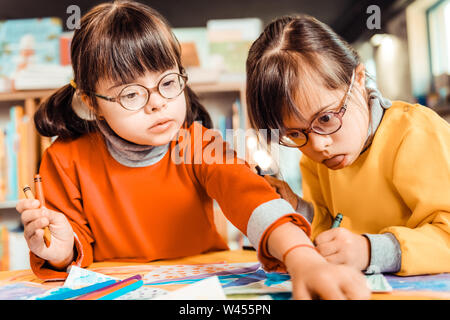 Curioso ragazza dai capelli scuri in occhiali tenendo il nuovo colore della matita Foto Stock