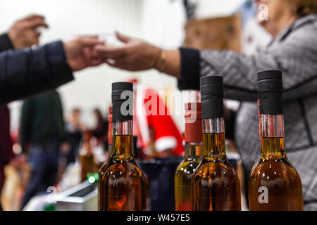 Bottiglie di homebrewed vin brulé sono visti da vicino ad una esposizione di Natale, un acquirente è visto lo scambio di denaro con un venditore, sfocata in background. Foto Stock