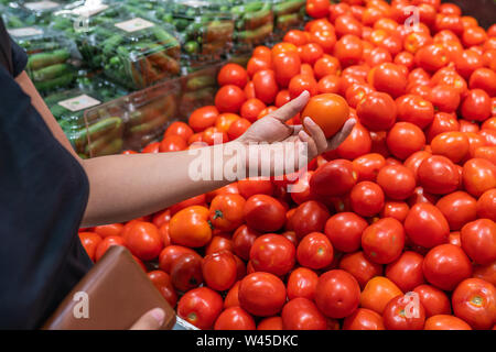 Close up foto di donna raccolta a mano il pomodoro al negozio di alimentari Foto Stock