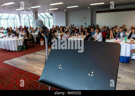 Un altoparlante stand della con microfono è osservata da vicino durante un pranzo conferenza per professionisti, sfocata i dipendenti sono visto seduto dietro. Foto Stock