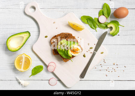 Toast con freschi maturi avocado, limone e uova sul bianco tavolo in legno, vista dall'alto composizione Foto Stock