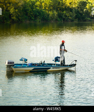 Un africano America uomo pesca dalla sua imbarcazione a motore al tramonto, nel mezzo del fiume nel sud-est USA, Foto Stock