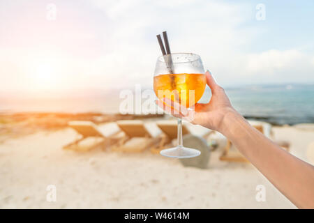 Donna che mantiene una deliziosa classic iced aperol spritz cocktail con cubetti di ghiaccio su una calda spiaggia tropicale in estate sole Foto Stock