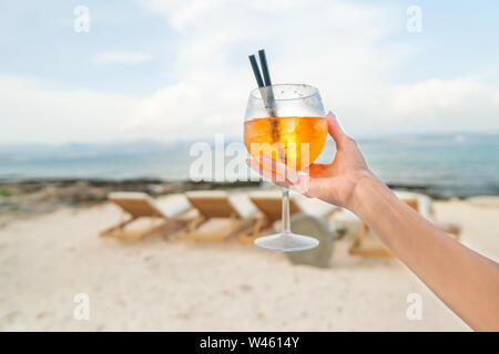 Donna che mantiene una deliziosa classic iced aperol spritz cocktail con cubetti di ghiaccio su una calda spiaggia tropicale in estate sole Foto Stock