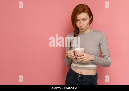 I Capelli rossi ragazza detiene una tazza e guardando la telecamera con faccia buffa espressione Foto Stock