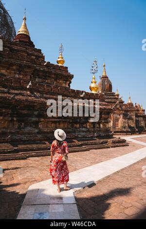 BAGAN, Myanmar (Birmania) - Mar 15, 2018: un colpo verticale di una femmina con un abito rosso camminare vicino a un tempio in una giornata di sole in Myanmar, ha iniziato Foto Stock