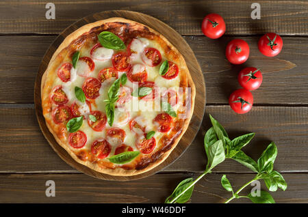 La Pizza Margherita su un tagliere, pomodoro fresco e basilico sul tavolo di legno, vista dall'alto Foto Stock