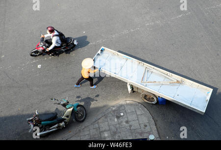 Vista superiore femmina di rottame di ferro il concessionario spingere lungo foglio su carrello a piedi sulla strada a Ho Chi Minh City, Vietnam il giorno Foto Stock