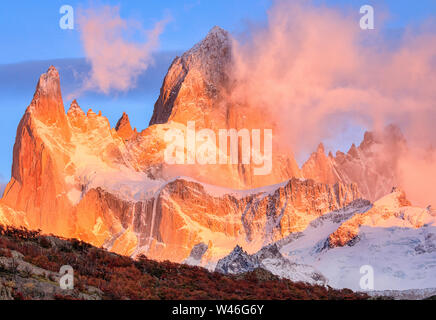 Il colore rosso brillante picco di Mount Fitzroy all'alba. Nuvole rosa e azzurro del cielo. Parco nazionale Los Glaciares. El Chalten. Ande. Foto Stock