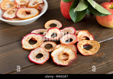 Essiccato anelli di Apple su un tavolo di legno, essiccati in anelli di mela nella ciotola e mele fresche sulla tavola Foto Stock