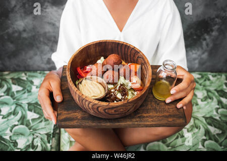 Donna di mangiare falafel sfere, hummus e insalata fresca nella ciotola di legno. Arabo tradizionale orientale, o cibo israeliano. Il veganismo concetto. Foto Stock