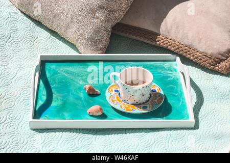 Primo piano di una tazza decorata con caffè in essa piccole conchiglie sul lato di un vassoio blu Foto Stock