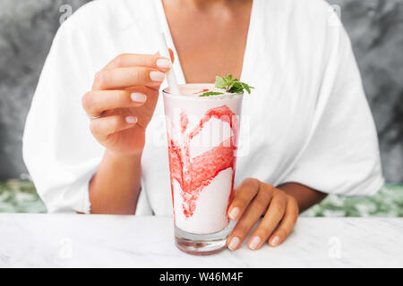 Donna di bere freschi e saporiti di latte freddo agitare con rosso di sciroppo di fragola. Il frappuccino dolce bevanda. Bevanda estiva concetto. Foto Stock