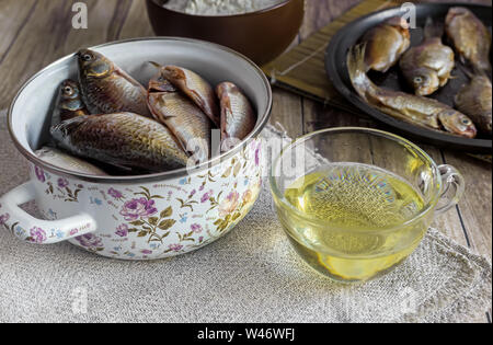 Sul tavolo è cucinato per la frittura di pesce di fiume, vicino a olio e farina di pesce, già fritti in padella. Foto Stock