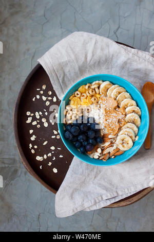 Sana di fiocchi d'avena e delizioso con mirtilli, banana, mandorle, noci di cocco, peanuut burro e cereali sulla piastra di stile rustico. Foto Stock