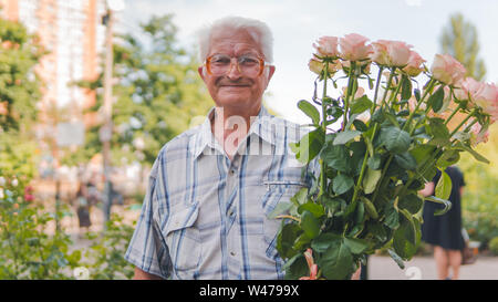 Ritratto di un uomo anziano in piedi sulla strada con un bouquet di rose. Close-up verticale sul vecchio uomo, all'aperto Foto Stock