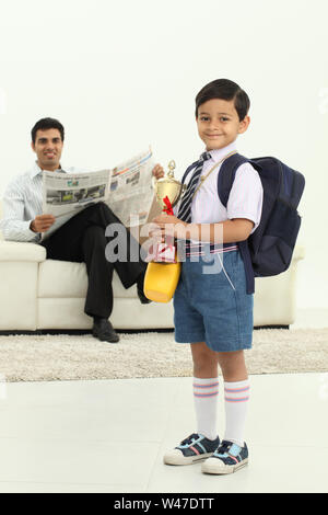 Scolaro che tiene un trofeo con suo padre che legge giornale dentro lo sfondo Foto Stock