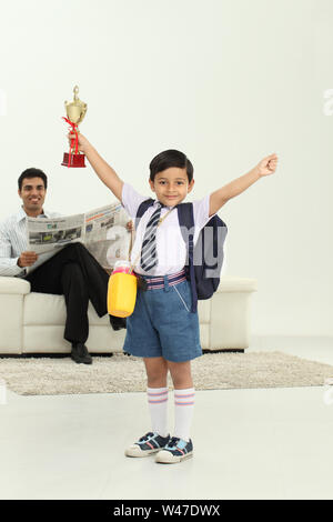 Scolaro che tiene un trofeo con suo padre che legge giornale dentro lo sfondo Foto Stock