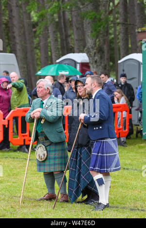 Tomintoul, Scozia. Il 20 luglio 2019 uno dei più importanti giochi delle Highland Gathering iniziò con la tradizionale sfilata delle locali bande di cornamuse attraverso la cittadina di Tomintoul e ha ringraziato la gente del posto a diverse fermate lungo la strada che hanno fornito una DRAM di locale lo scotch whisky per ogni membro della band. Nonostante la pioggia pesante, i giochi hanno continuato di intrattenimento per migliaia di spettatori compresi molti turisti provenienti da paesi stranieri Foto Stock