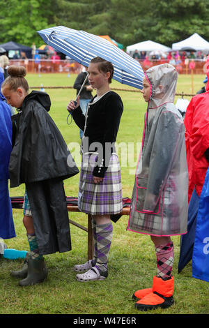 Tomintoul, Scozia. Il 20 luglio 2019 uno dei più importanti giochi delle Highland Gathering iniziò con la tradizionale sfilata delle locali bande di cornamuse attraverso la cittadina di Tomintoul e ha ringraziato la gente del posto a diverse fermate lungo la strada che hanno fornito una DRAM di locale lo scotch whisky per ogni membro della band. Nonostante la pioggia pesante, i giochi hanno continuato di intrattenimento per migliaia di spettatori compresi molti turisti provenienti da paesi stranieri Foto Stock