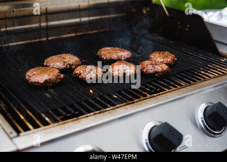 Hamburger essendo cotti su una griglia d'estate. Foto Stock