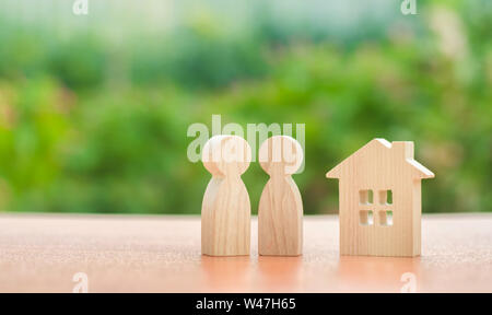 Due figure in legno di persone e una casa su un sfondo natura. concetto di alloggi accessibili, mutui per acquistare una casa per le giovani famiglie e cou Foto Stock