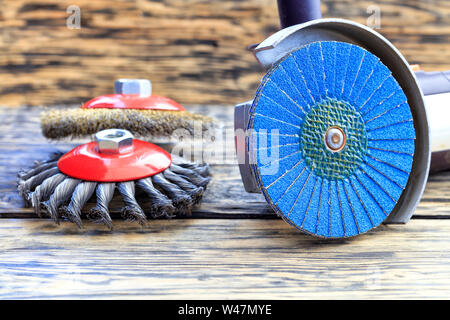 Molatrice angolare con disco di rettifica delle spazzole e abrasivi spazzole di filo si trova sullo sfondo di un tavolo di legno. Foto Stock