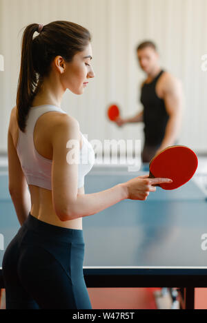 L uomo e la donna a giocare a ping pong all'interno. Matura in sportswear trattiene le racchette e gioca a tennis da tavolo in palestra Foto Stock