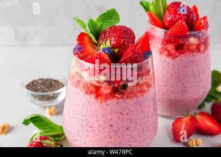Yogurt alla fragola con chia semi, frutti di bosco freschi, granola e menta per una sana colazione gustosa su marmo bianco sullo sfondo Foto Stock