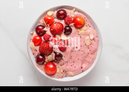 Ciotola frullato o Nizza crema fatta di banane surgelate e frutti di bosco con frutti di bosco freschi, noci e semi su marmo bianco tavola. Colazione sana. vista superiore Foto Stock