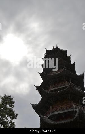 Guardando verso l'alto un alto, ornati, cinese tradizionale pagoda. Stagliano contro un luminoso cielo grigio, il sole nascosto dietro le nuvole, appuntiti angoli di balc Foto Stock